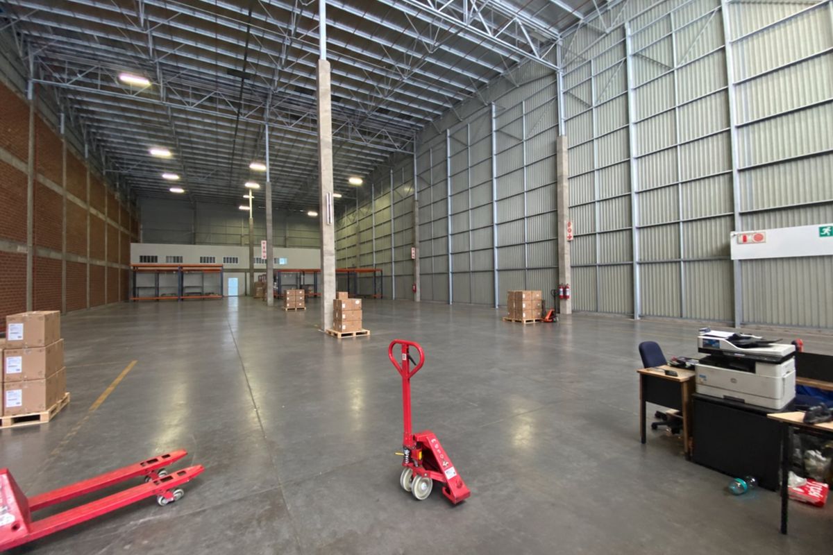 Spacious industrial warehouse featuring high ceilings with exposed steel trusses, polished concrete flooring, and metal wall cladding, suitable for storage or logistics operations.