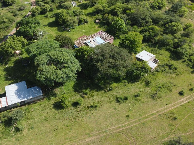 Aerial view of a large vacant commercial land parcel featuring multiple structures with damaged roofing and extensive surrounding vegetation.