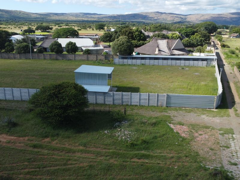 Aerial view of a vacant commercial plot featuring perimeter precast concrete walling and a small metal storage structure.