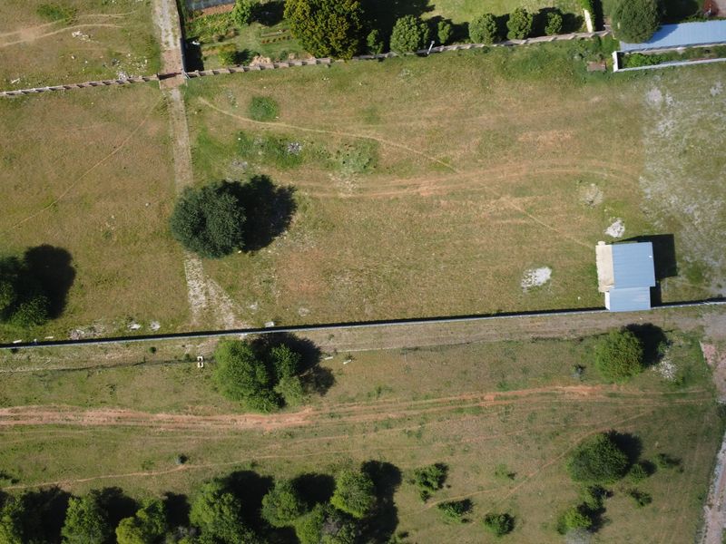 Aerial view of a vacant commercial land plot featuring perimeter fencing, mature trees, and a small existing outbuilding structure.