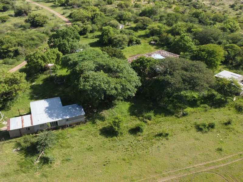Aerial view of a large vacant commercial land plot featuring mature trees, dirt access tracks, and existing structures with incomplete roofing.