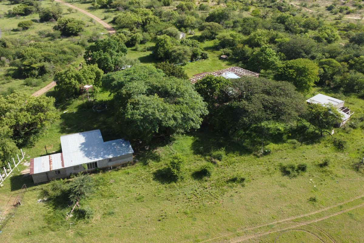 Aerial view of a large vacant commercial land plot featuring mature trees, dirt access tracks, and existing structures with incomplete roofing.