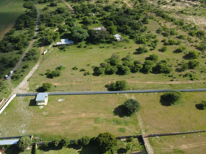 Aerial view of a large vacant commercial land plot featuring perimeter fencing, scattered trees, and a small utility structure on the property.