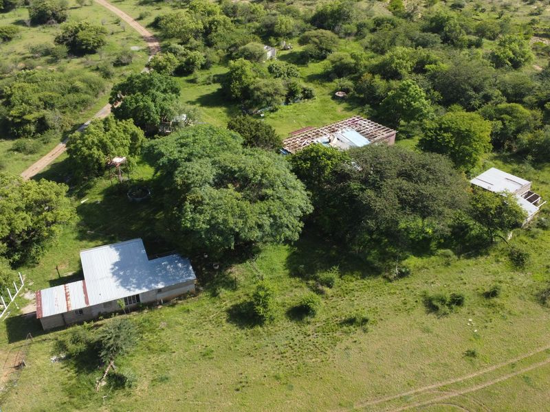 Aerial view of a vacant commercial land plot featuring multiple structures with varying states of roof completion and surrounding natural vegetation.