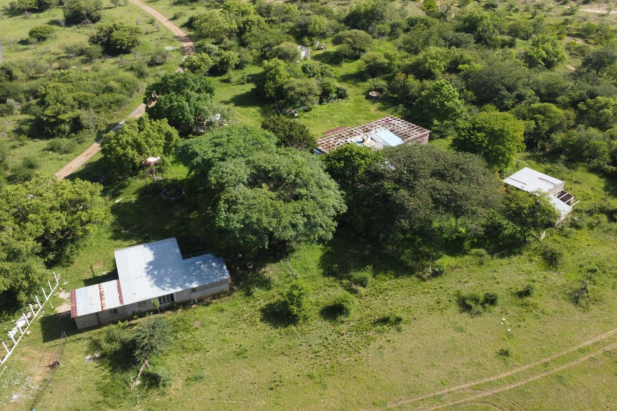 Aerial view of a vacant commercial land plot featuring multiple structures with varying states of roof completion and surrounding natural vegetation.