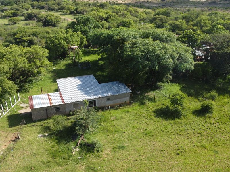 Aerial view of a commercial vacant land plot featuring a single-story brick structure with a corrugated metal roof and surrounding natural vegetation.