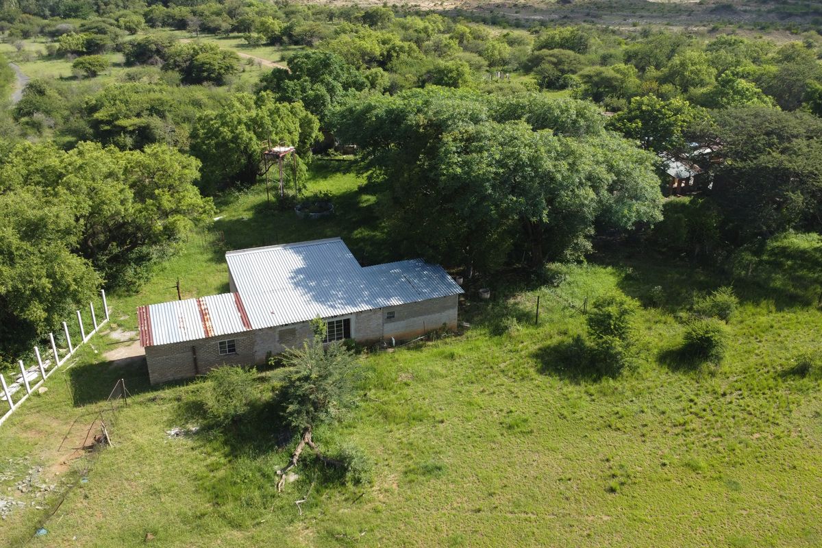 Aerial view of a commercial vacant land plot featuring a single-story brick structure with a corrugated metal roof and surrounding natural vegetation.