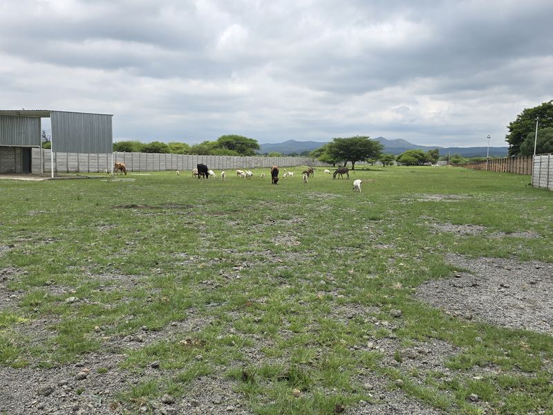 A large, open commercial vacant land plot enclosed by perimeter concrete block walls, featuring a metal storage structure and expansive grassy terrain.