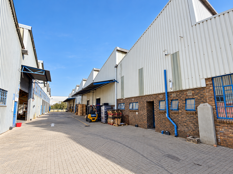 Exterior view of an industrial warehouse complex featuring corrugated metal cladding, face brick walls, and a paved loading area.