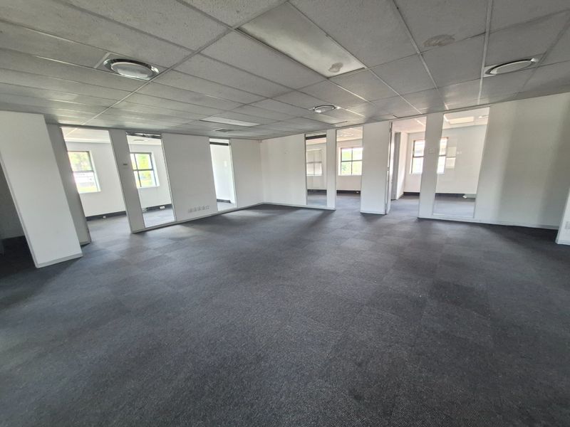 Spacious open-plan office area featuring a suspended ceiling, recessed lighting, and carpet tiles, with multiple partitioned office spaces visible.