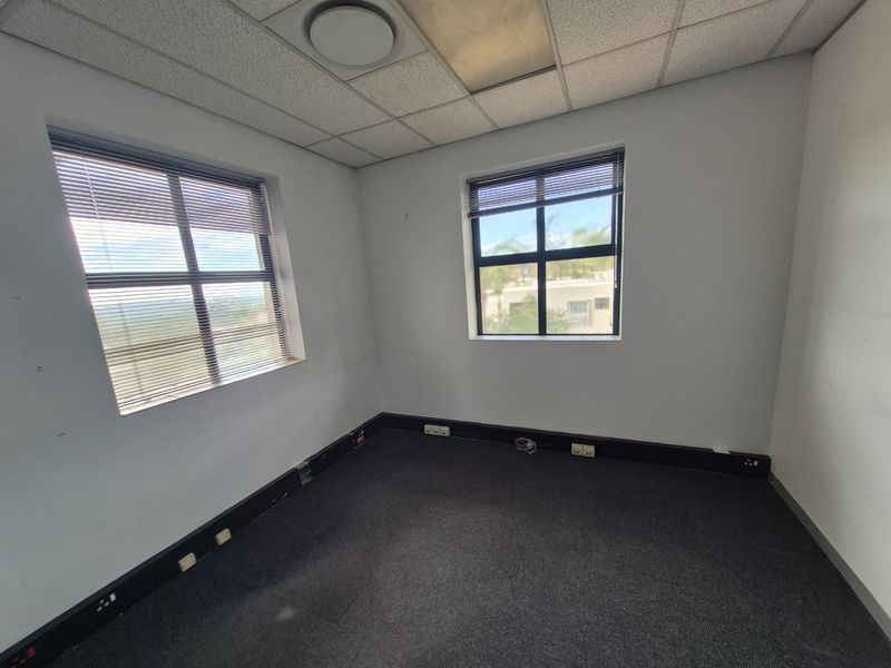 A vacant office space featuring a suspended ceiling, carpeted flooring, and integrated power trunking along the baseboards with natural light from two windows.
