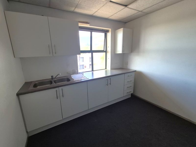 A functional office kitchenette featuring white built-in cabinetry, a laminate countertop, and a stainless steel double sink under a drop ceiling.