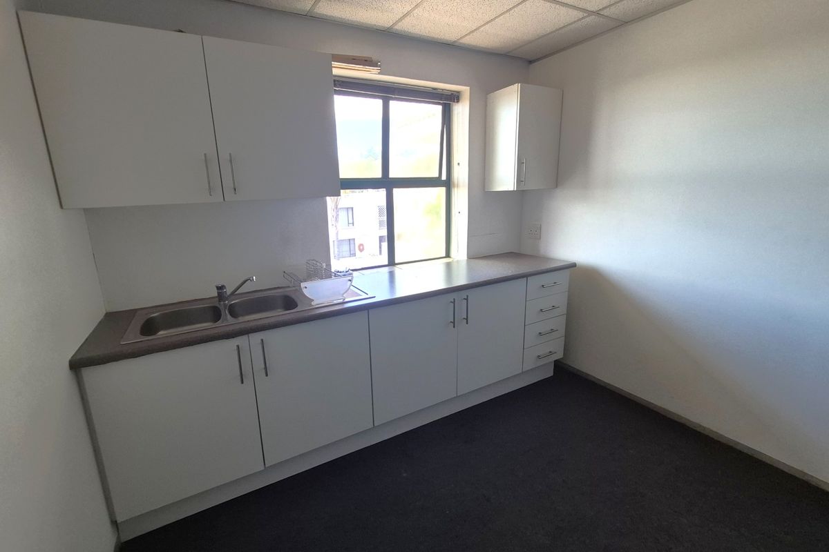 A functional office kitchenette featuring white built-in cabinetry, a laminate countertop, and a stainless steel double sink under a drop ceiling.