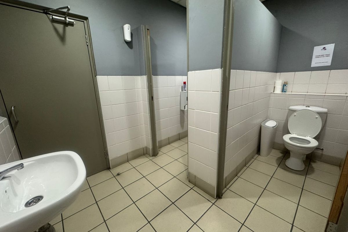 Functional industrial restroom facility featuring tiled flooring, partitioned toilet cubicles, and a wall-mounted basin.