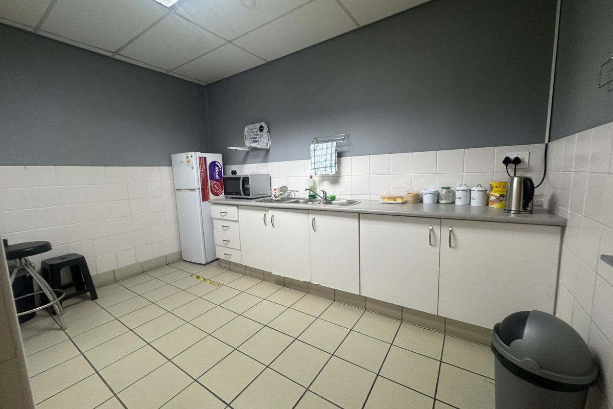 A functional industrial kitchenette featuring white cabinetry, a stainless steel sink, tiled splashbacks, and a drop ceiling with integrated lighting.