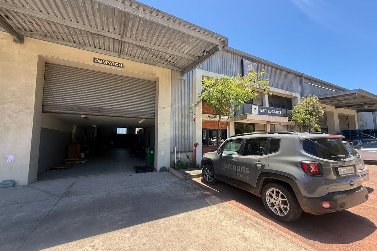 Industrial warehouse unit featuring a large roller shutter door for dispatch, metal cladding, and dedicated access point in a functional logistics park setting.