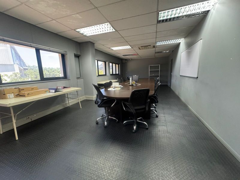 A functional industrial office space featuring a large boardroom table, recessed ceiling lighting, and durable rubberized flooring.