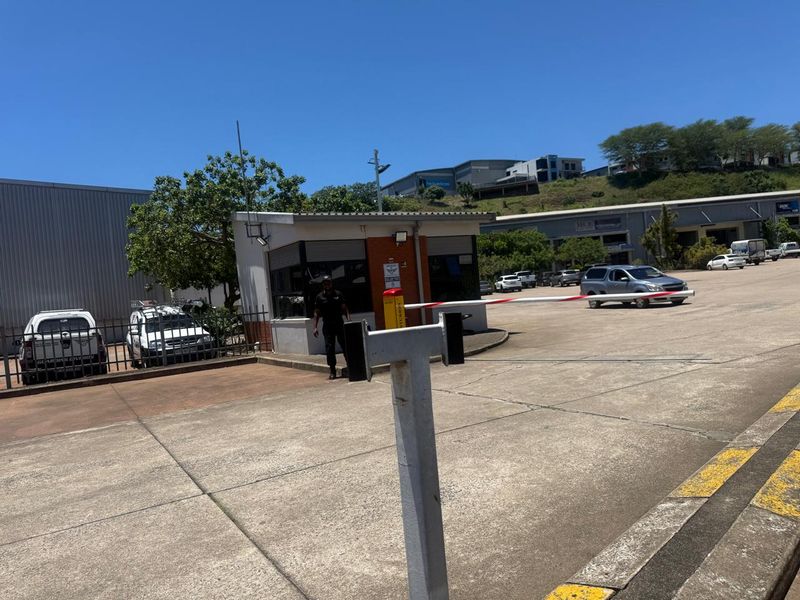 Industrial property entrance featuring a security guard booth, boom gate access control, and paved yard area.