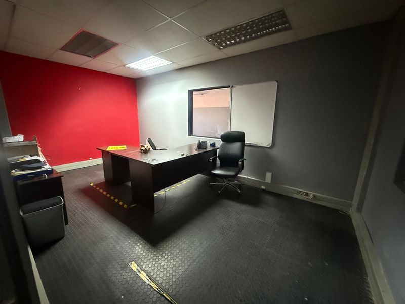 A functional office space featuring a drop ceiling with recessed lighting, rubberized flooring, and a large interior viewing window.