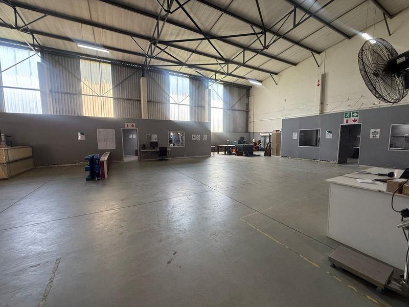 Spacious industrial warehouse featuring high-clearance ceilings, exposed steel trusses, polished concrete flooring, and multiple partitioned office or utility access points.