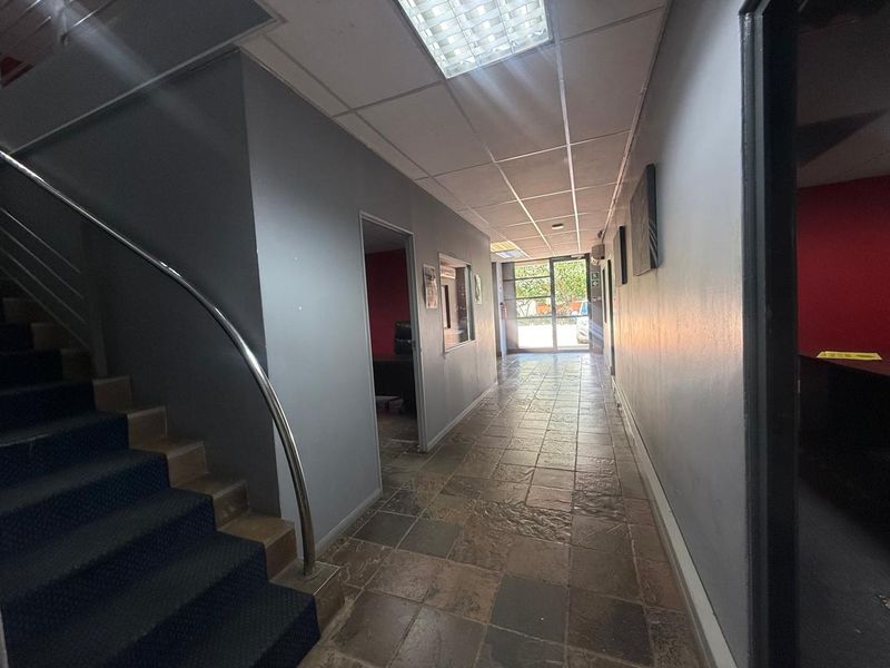 A functional industrial office hallway featuring tiled flooring, a metal staircase with a handrail, and access to multiple office rooms.