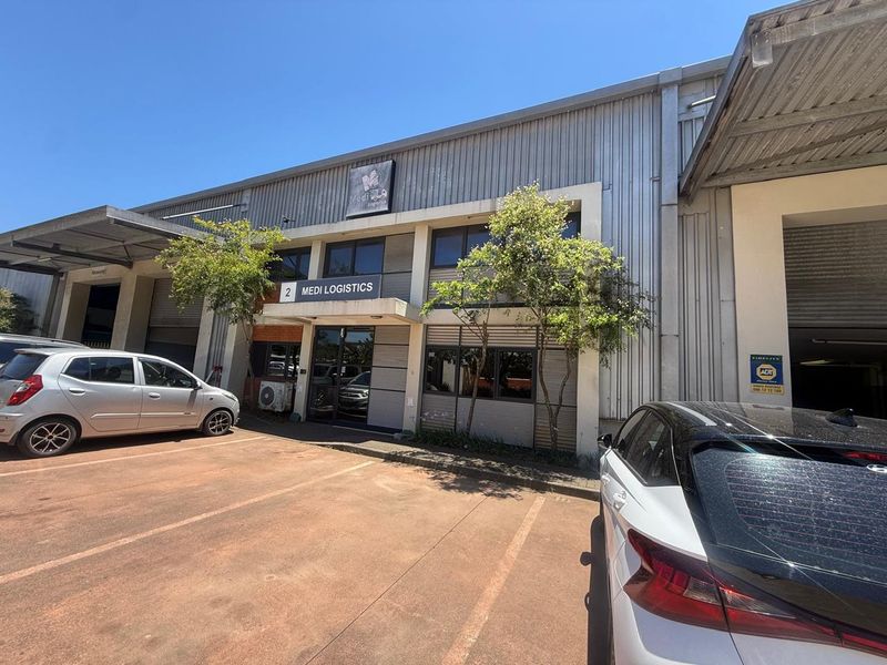 Industrial warehouse unit featuring a metal facade, glass entrance doors, and dedicated parking space in a functional business park setting.