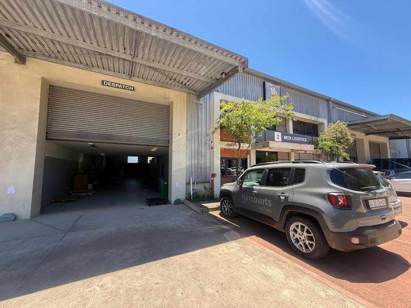 Industrial warehouse unit featuring a large roller shutter door for dispatch, metal cladding, and dedicated access point in a functional logistics park setting.