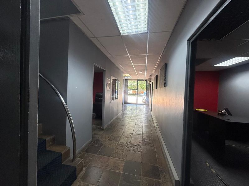 A functional industrial hallway featuring tiled flooring, recessed ceiling lighting, and access to multiple office spaces with a staircase leading to the upper level.