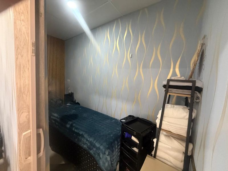 A compact treatment room featuring decorative patterned wallpaper and vertical timber slat wall paneling, suitable for a salon or wellness retail space.