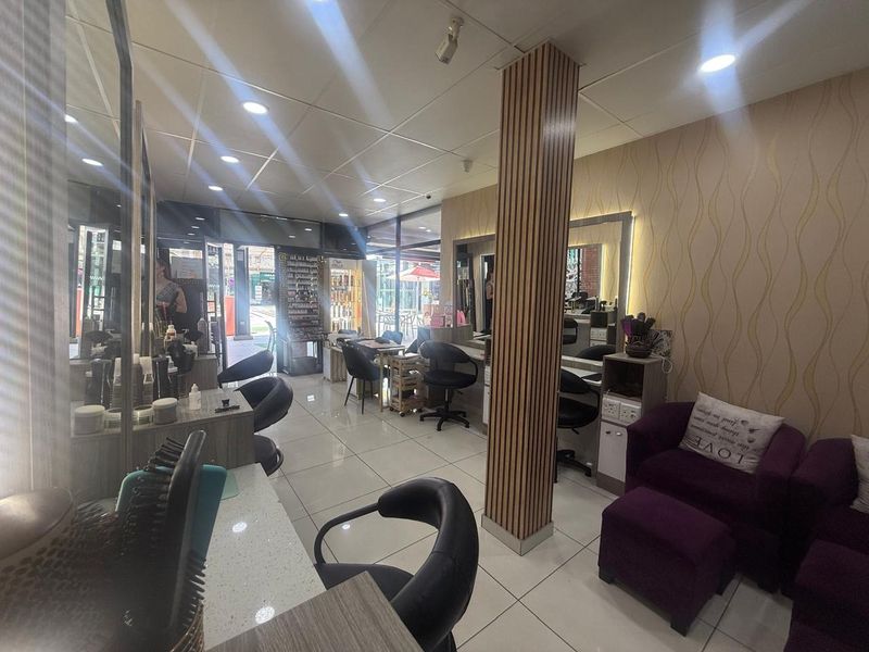 A well-lit retail salon space featuring tiled flooring, recessed ceiling lighting, and multiple built-in styling stations with integrated mirrors.