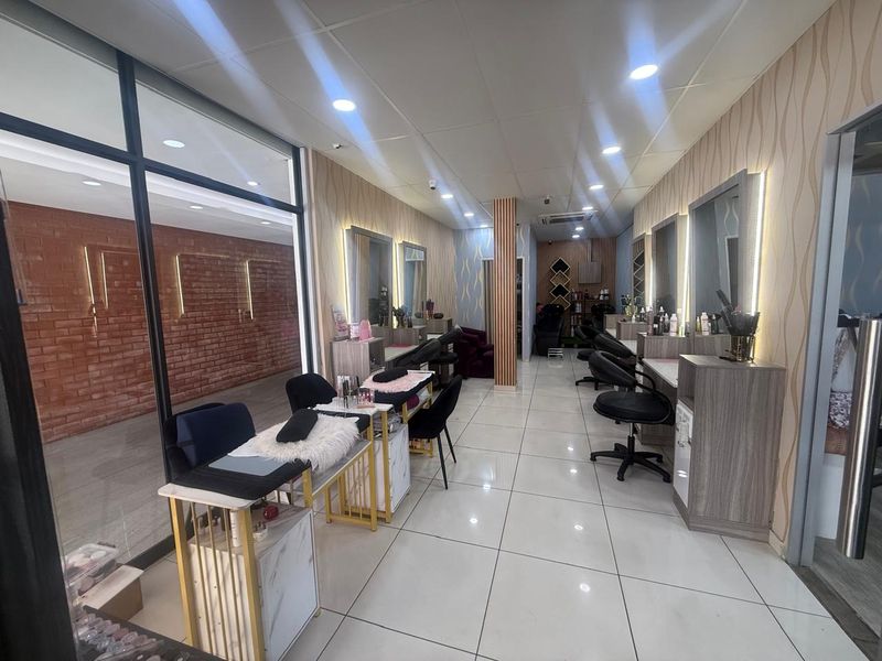 A well-maintained commercial salon space featuring tiled flooring, recessed ceiling lighting, and multiple built-in vanity stations with integrated mirrors and lighting.