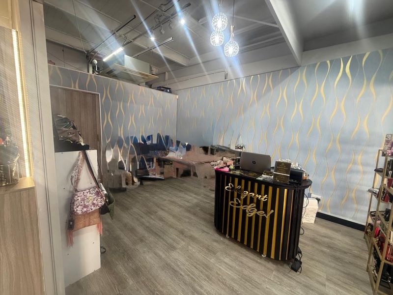 A retail interior space featuring wood-look flooring, decorative patterned wallpaper, exposed ceiling structure with track lighting, and a central service counter.
