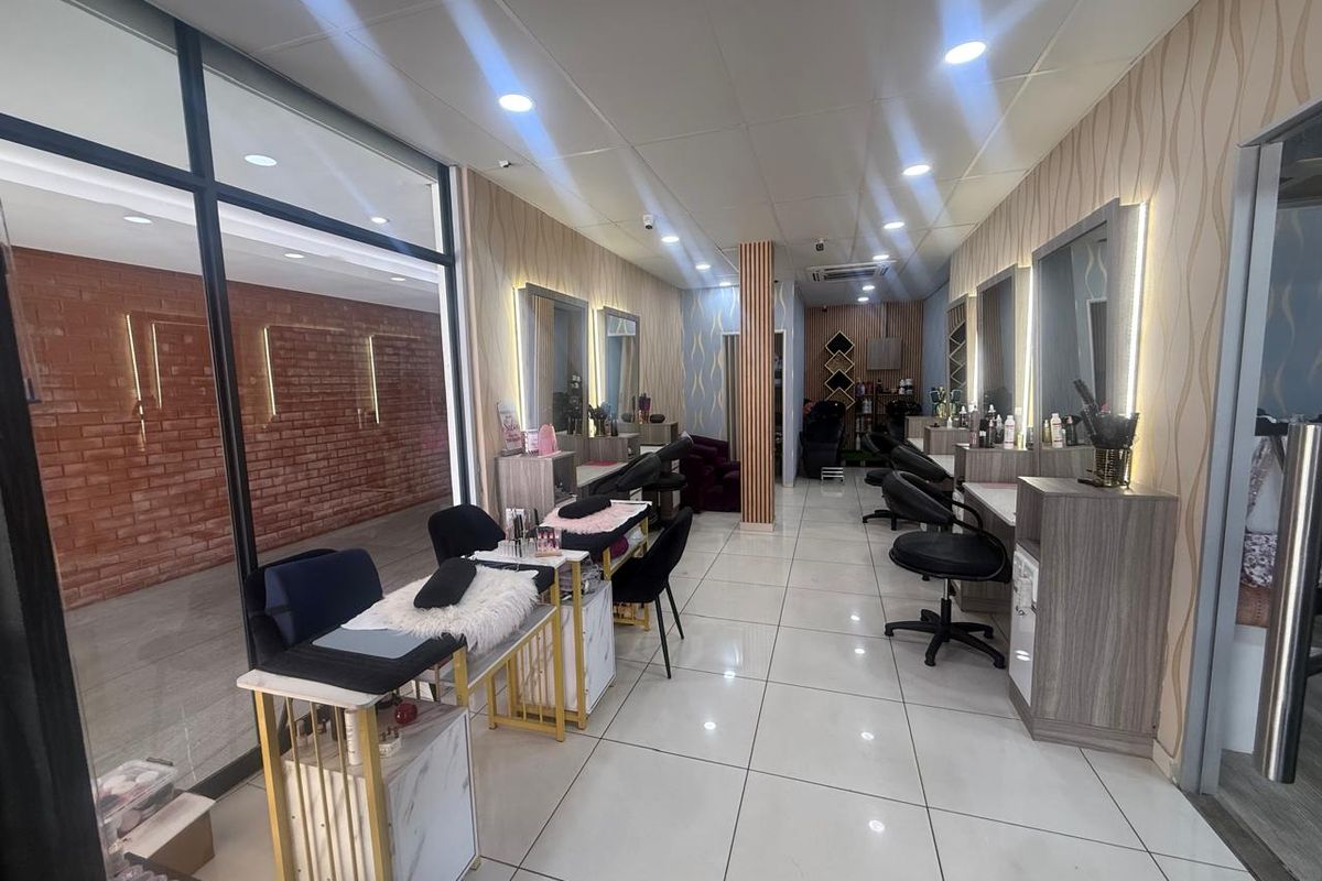 A well-maintained commercial salon space featuring tiled flooring, recessed ceiling lighting, and multiple built-in vanity stations with integrated mirrors and lighting.