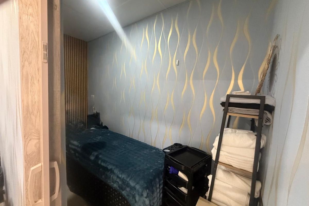 A compact treatment room featuring decorative patterned wallpaper and vertical timber slat wall paneling, suitable for a salon or wellness retail space.