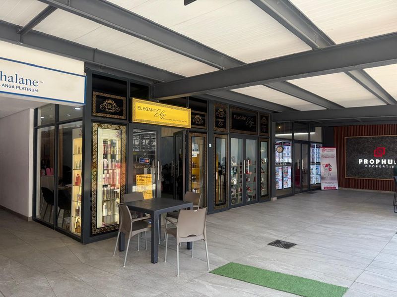 A modern retail storefront featuring glass-fronted display windows, metal framing, and a covered walkway area with tiled flooring.