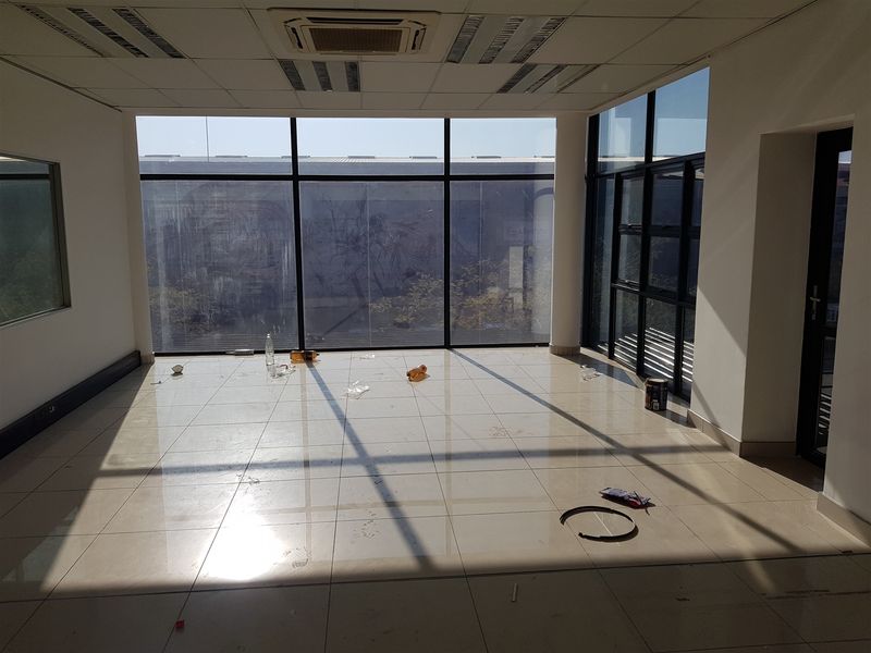 An empty, sunlit office space featuring large floor-to-ceiling windows, tiled flooring, and integrated ceiling air conditioning.
