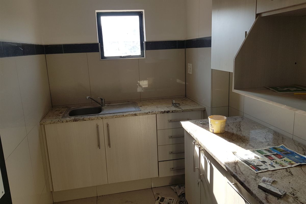 A functional kitchen area featuring granite countertops, built-in cabinetry, and a stainless steel sink with tiled wall finishes.