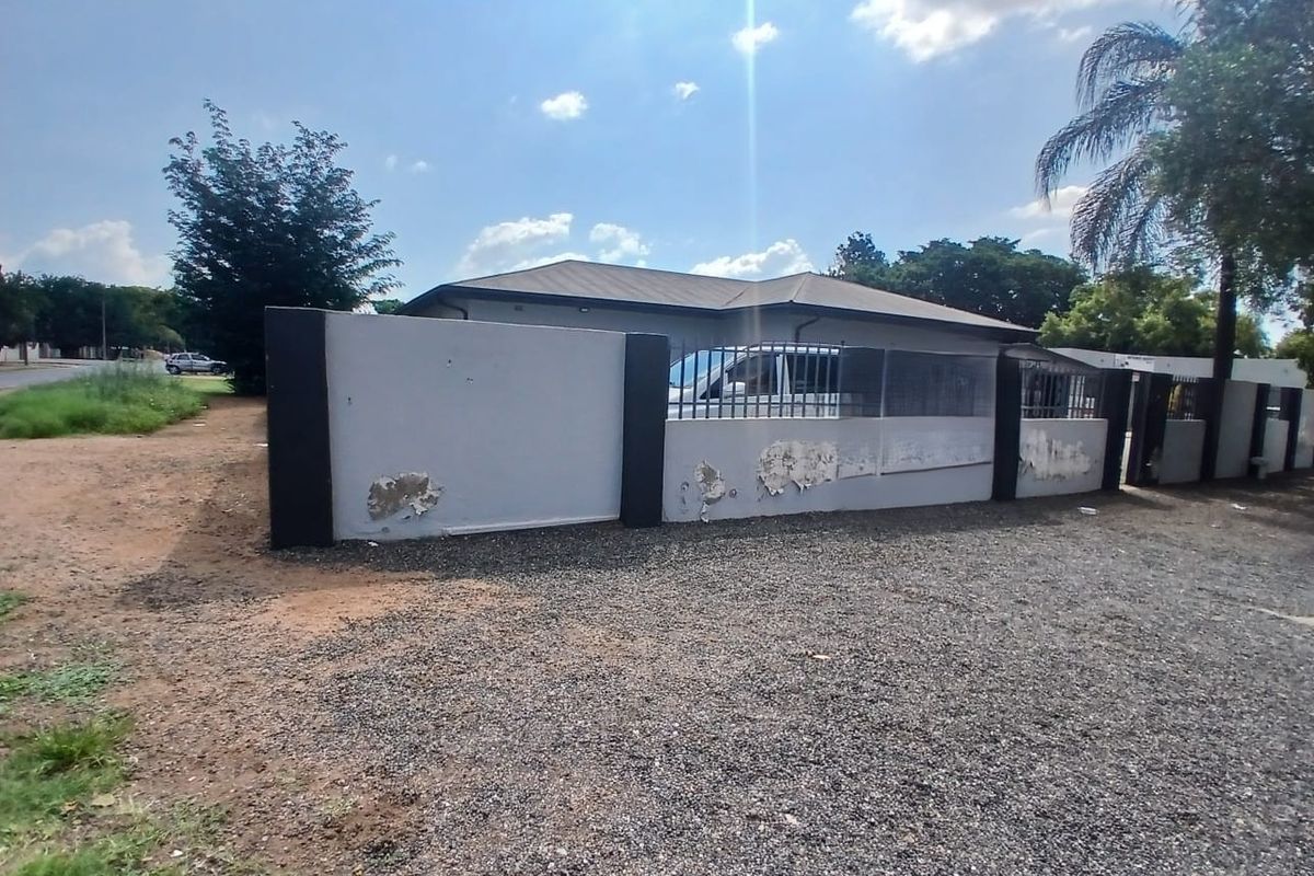 Exterior view of the property featuring a perimeter boundary wall with metal fencing and a gravel driveway area.