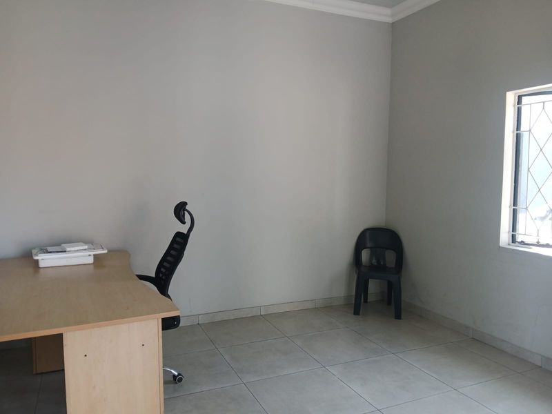 A functional office space featuring neutral tiled flooring, plain walls, and a window with security bars.
