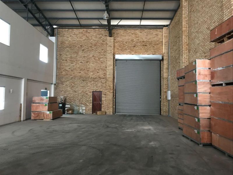 Spacious industrial warehouse unit featuring high ceilings with exposed steel trusses, durable concrete flooring, and a large roller shutter door for easy access.