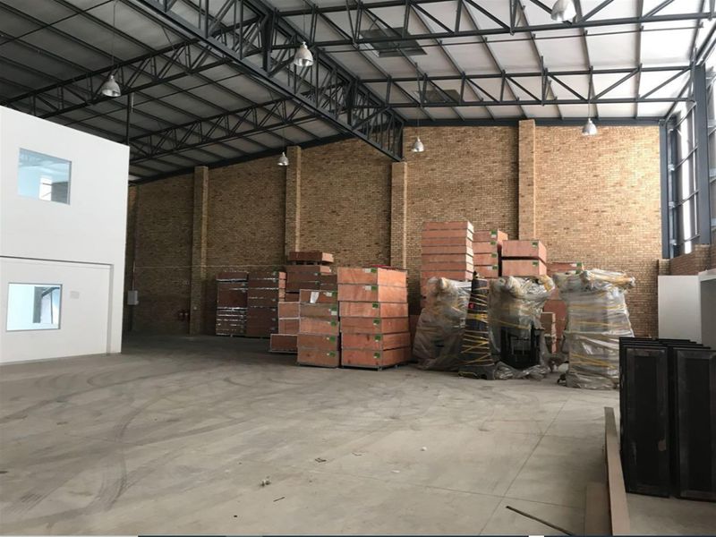 Spacious industrial warehouse featuring high exposed steel roof trusses, durable concrete flooring, and exposed brick walls with an integrated mezzanine office area.