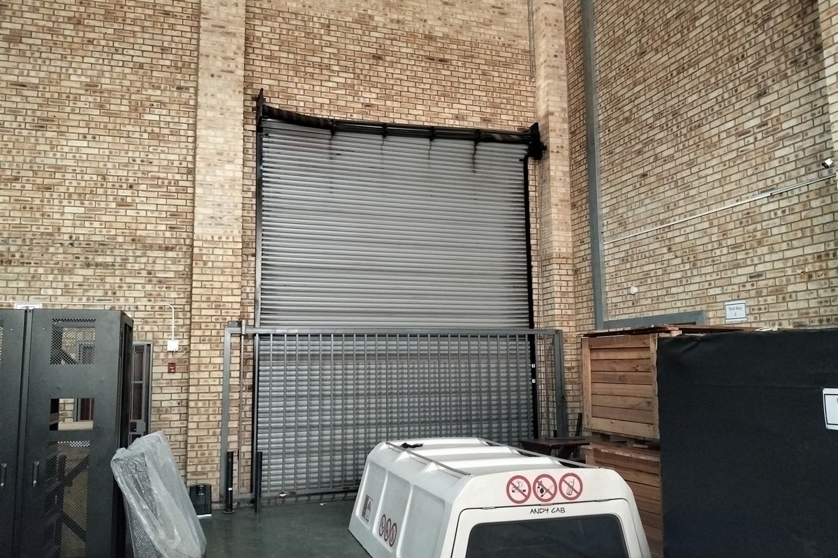 Industrial utility space featuring high exposed brick walls and a large roller shutter door with an integrated metal security gate.