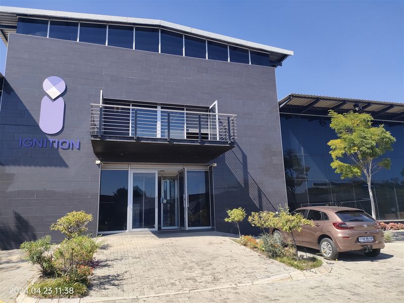 Modern industrial office building featuring a dark tiled facade, glass entrance, and a metal balcony, set within a well-maintained commercial property.