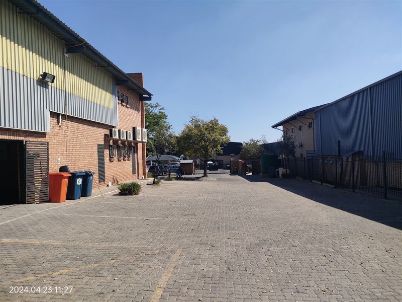 An industrial exterior view showing a paved yard area between two warehouse buildings with brick and metal cladding finishes.