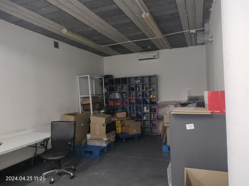 A functional industrial utility or storage space featuring an exposed concrete ceiling, wall-mounted air conditioning, and basic lighting fixtures.