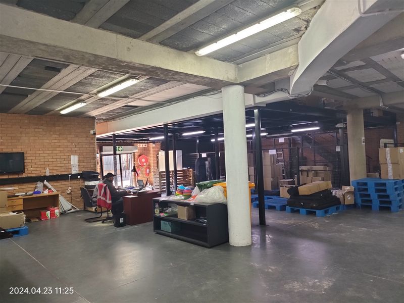 Spacious industrial utility area featuring exposed concrete ceilings, brick walls, and a mezzanine level, suitable for warehouse or workshop operations.