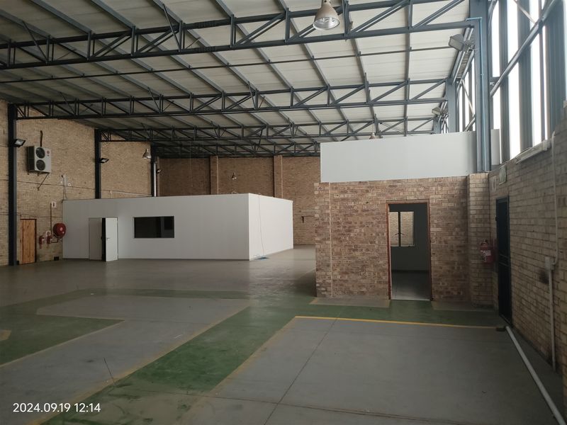 Spacious industrial warehouse featuring exposed brick walls, high steel roof trusses, concrete flooring, and a dedicated internal office partition.
