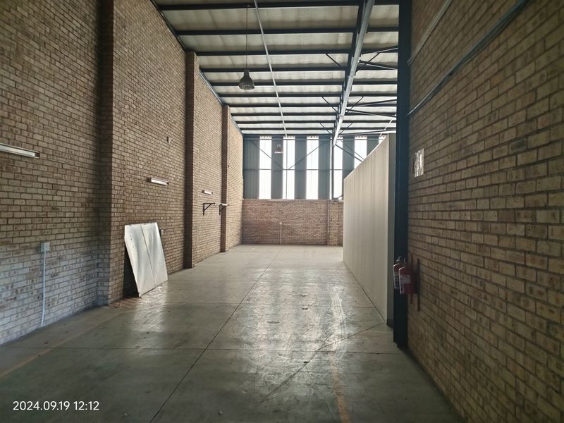 Spacious industrial utility area featuring exposed brick walls, concrete flooring, and high-clearance steel roof trusses, suitable for storage or workshop use.