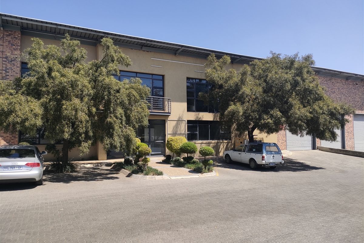 Front elevation of an industrial property featuring a brick and plaster facade, large windows, a small balcony, and paved driveway access with roller shutter doors.