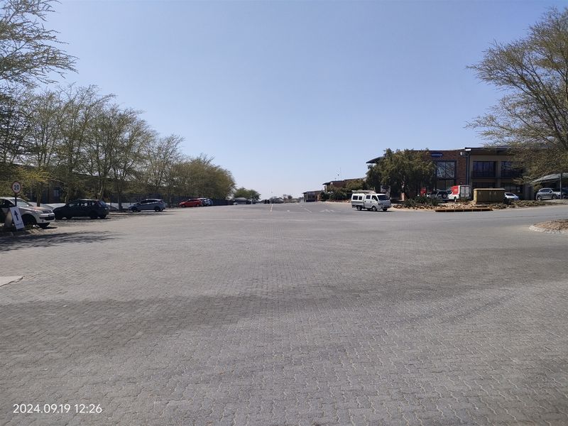 A wide-angle view of a paved industrial parking lot and driveway area with surrounding trees and commercial building access.
